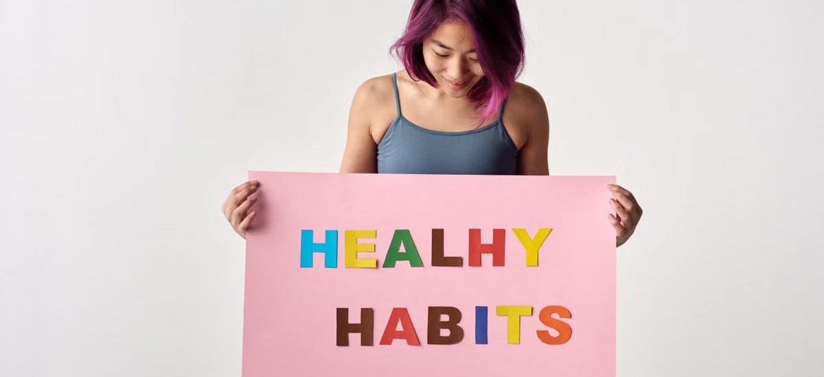 Asian woman holding a colorful 'Healthy Habits' sign in a studio setting, promoting wellness.