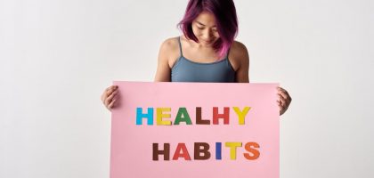Asian woman holding a colorful 'Healthy Habits' sign in a studio setting, promoting wellness.