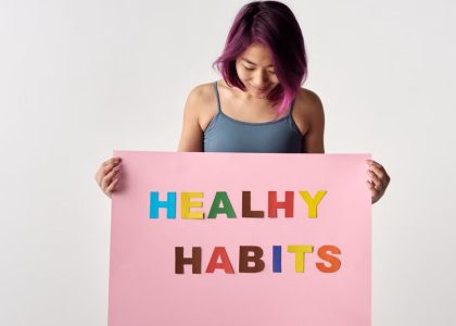 Asian woman holding a colorful 'Healthy Habits' sign in a studio setting, promoting wellness.