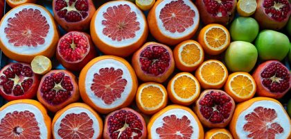 A colorful arrangement of sliced citrus fruits and pomegranates in a street market setting.