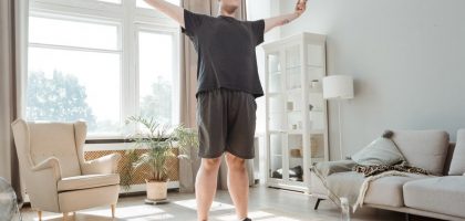 A man performs a stretching exercise with arms out in a bright, modern living room.