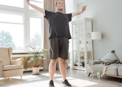 A man performs a stretching exercise with arms out in a bright, modern living room.